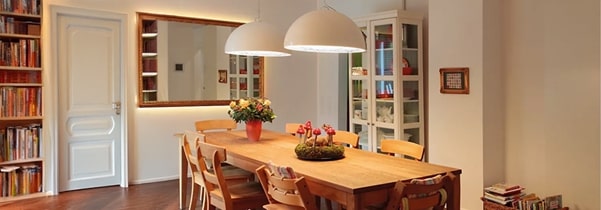 A dining room with two large white pendant lights hanging above a wooden dining table.